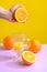 Oranges, a transparent glass and a juicer. Bright background, creative frame, fashion light. Purple and yellow. The concept of