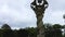 orbit footage of a tall slender wooden sculpture in the garden surrounded by lush green trees on a cloudy day at Callaway Gardens