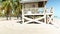 orbit footage of a white wooden lifeguard tower on a sandy white beach with lush green palm trees and blue ocean water