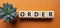 Order symbol. Wooden cubes with word Order. Beautiful orange background with succulent plant. Business and Order concept. Copy