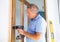 Ordinary elderly man screwing door hinges with screwdriver to new wooden door
