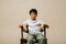 Ordinary indian boy sitting on an armchair in a room over beige background