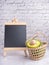 Organic avocado with seed, avocado halves in a basket, and a small blackboard on a marble background with a white brick wall. Side