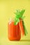 Organic carrot juice with carrots, celery on yellow background. Vegetable smothie in glass jar. Copy space. Summer food