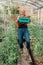 Organic female farmer having fun and fooling around box full of fresh produce on her farm. Happy young woman smiling at