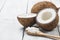 Organic natural whole and cracked coconut fruit and pieces of coconuts in wooden spoon on white wooden background