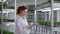 organic plants, portrait of female biologist wearing glasses and gloves examines young micro green plants in containers