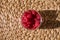 Organic raspberries in the glass on the natural straw table mat. Straw background. Healthy snack.