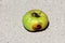 Organic ripe light green to yellow apple with large dark brown worm hole left on concrete in front of family house