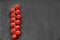 Organic ripe raw cherry tomatoes on a long branch on black texture background. Free space on the right side.