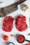 Organic rump steak, raw beef meat with seasonings, rosemary, garlic and butcher cleaver. White textured background. Top view