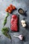 Organic Tri-tip, triangle roast marbled beef on black plate , marbled beef with herbs tomatoes peppercorns over grey stone surface