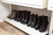 Organized shoe rack, shoe rack with black stylisch shoes and boots, on a wooden floor, besides a white wall. modern room