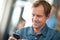 Organizing in todays business. a man sitting in an office messaging on a cellphone with colleagues in the background.