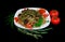 Oriental dish of fried meat with Dungan noodles in a white plate on a black background with greenery, hot pepper and tomatoes
