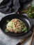 Oriental tabbouleh salad with couscous, vegetables and herbs in a black bowl on a gray background