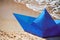 Origami blue paper boat on sandy beach for concept design, beautiful paper ship on shore, close up