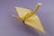 Origami in the form of a crane figurine own hand made folded from yellow thick paper on a purple background.