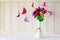 Origami paper flowers in vase and butterflies on white wooden wall.