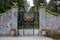 Ornament forged big iron garden gate at the stone wall. Gold and black