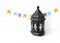 Ornamental dark Moroccan, Arabic lantern on the white table. Party decoration, string of colorful paper flags. Greeting