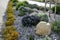 Ornamental flower bed with perennial pine and gray granite boulders, mulched bark and pebbles in an urban setting near the parking