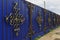 Ornate and beautiful wrought iron fence gate painted scarlet blue and gold. Close-up photo, shallow depth of field, blured