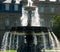 Ornate city fountain in light backlight in front of house facade