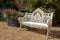 Ornate iron metal vintage retro garden seat, painted in white colour, located in rural garden with planter.