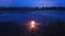 An ornate lantern glowing in the evening after sunset. On the ground, reflected in flood waters in a field on a winters evening.