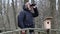 Ornithologist with binoculars and bird house in the park on the bridge