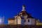 Orthodox Christian church with a golden dome at night is lit by a spotlight, a wooden cross is buried in the ground