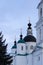 An orthodox white chirch with dark dome and golden crosses on top. A pine in the left corner