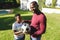 ortrait of smiling african american father with son embracing and holding football in sunny garden