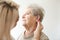 Otolaryngologist putting hearing aid in senior woman\'s ear on light background