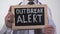 Outbreak alert text written on blackboard in doctor hands, epidemic warning
