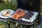 Outdoor barbecues. Sausages, black pudding, onions and baked bread on the grill. Food baked on aluminum foil tray