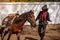 In an outdoor barn, one man dressed as a cowboy trains his horse to run in a circle around him