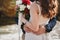Outdoor beach wedding ceremony near the ocean, close up of embrace of stylish couple with wedding bouquet, man is hugging bride
