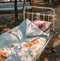 An outdoor bed in an autumn park with a bedspread and pillow and fallen foliage.