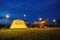 Outdoor camping tent with tarp or flysheet on grass courtyard and warm night light under dark blue sky twilight time, family