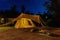 Outdoor camping tent with tarp or flysheet on grass courtyard and warm night light under dark blue sky twilight time, family