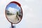 Outdoor convex safety mirror hanging on wall with reflection of an urban roadside view of cars parked along the street