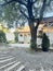 Outdoor exterior of summer vacation home. There are light buildings, pots of flowers near the doors and old tree with ivy.