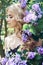 Outdoor fashion beautiful young woman surrounded by lilac flowers summer. Spring blossom lilac bush. Portrait of a girl blond
