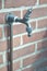 Outdoor faucet on a brick wall with a hose fitting attached.