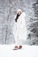 Outdoor full body portrait of beautiful fashionable woman wearing stylish white winter puffer coat, knitted hat, mittens, leggings