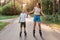 Outdoor full length portrait of happy brunette female holding son`s hand and rollerblading together, family wearing casual style