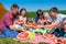 Outdoor group portrait of happy company having picnic near the tent in park and enjoying watermelon