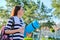 Outdoor happy mature woman walking after fit exercises in park, with backpack, yoga mat